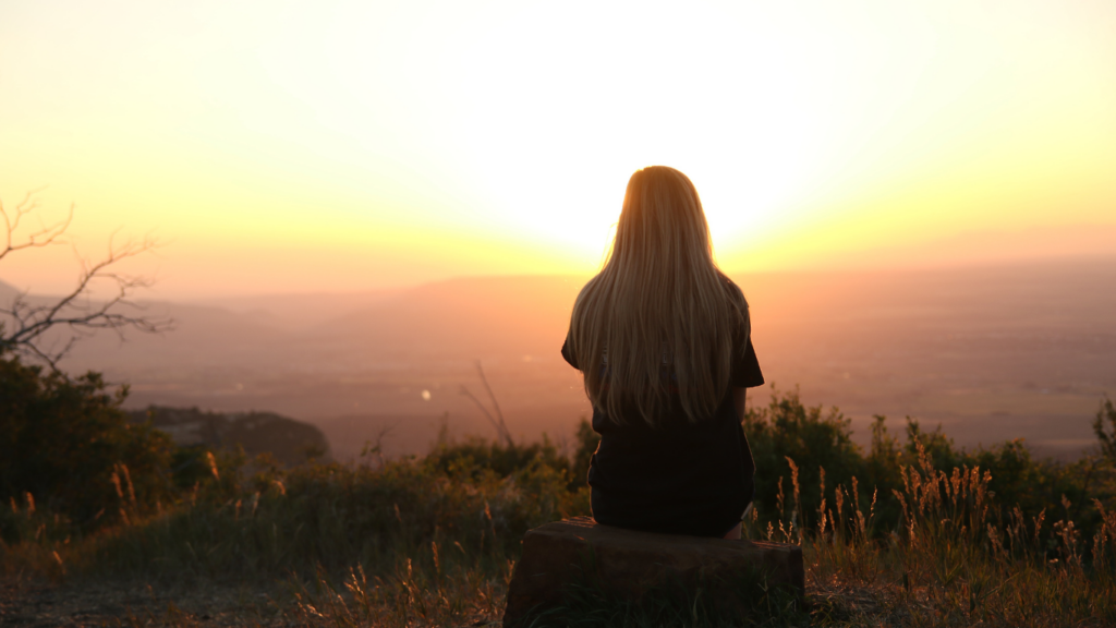 Girl sitting on a mountain top with the sunset in the background