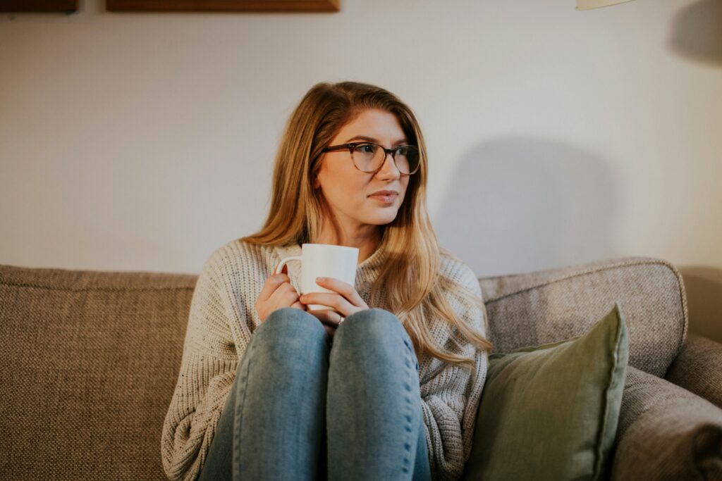 Woman sitting on a sofa with her knees up to her chest and coffee cup in her hand