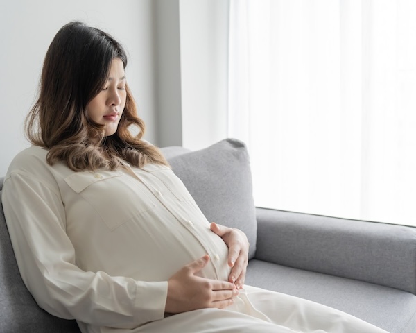 Young pregnant girl sitting on the sofa holding her tummy
